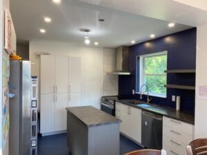 Cuisine moderne et élégante dans une maison de chambres dotée d'armoires blanches éclairées par des spots intégrés avec îlot central et appareils en acier inoxydable.