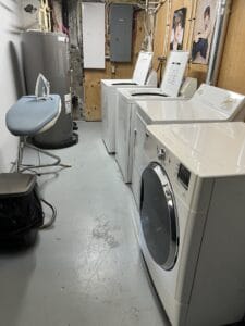 Buanderie moderne avec laveuses et sécheuses blanches bien alignées sur un sol gris offrant un espace fonctionnel et organisé pour vos besoins de lessive.