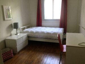 Chambre lumineuse et moderne avec lit double confortable, bureau et chaise, idéale pour le travail ou le repos, offrant une ambiance paisible avec parquet en bois.