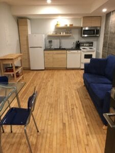 Appartement étudiant moderne avec cuisine équipée incluant réfrigérateur four micro-ondes et salon confortable avec canapé bleu et table en verre fauteuils bleus.